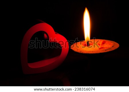A burning candle and red heart in dark.