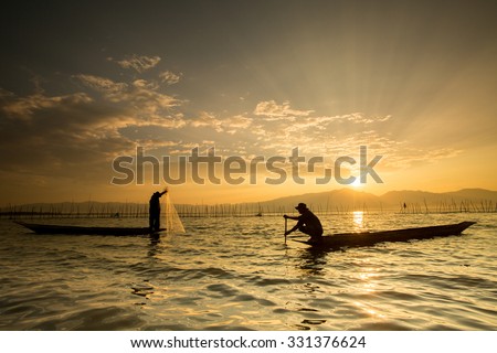 Silhouettes of the traditional fishermen throwing fishing net during sunrise, Thailand