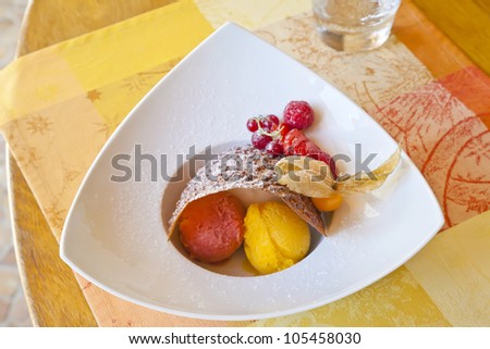 Raspberry and mango sorbet covered with a thin, arched cookie and decorated with gooseberry, strawberry, and raspberry, and served on a white plate.