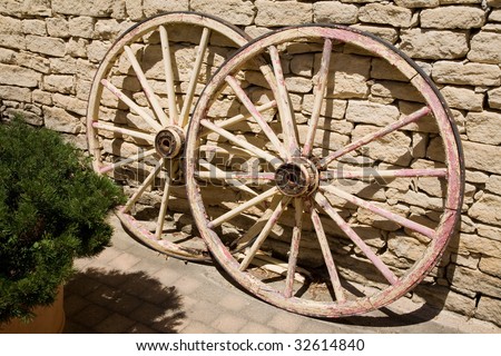 Two vintage wagon wheels against a rough stone wall.