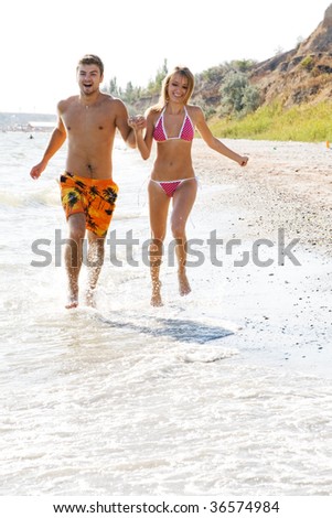 Young cheerful couple running along the beach
