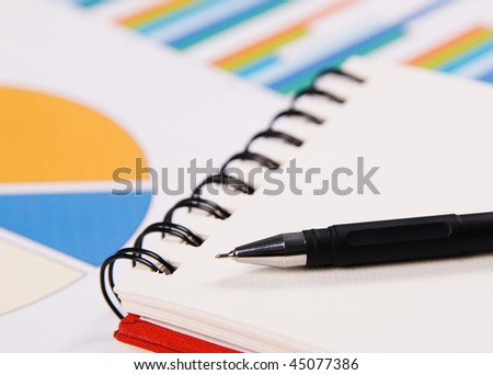 Close-up photo of a notebook and pen, with charts and diagrams on background