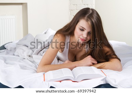 Young beautiful woman reading a book in bed