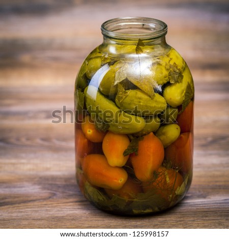 Pickles and tomatoes canned in a glass jar on wooden table