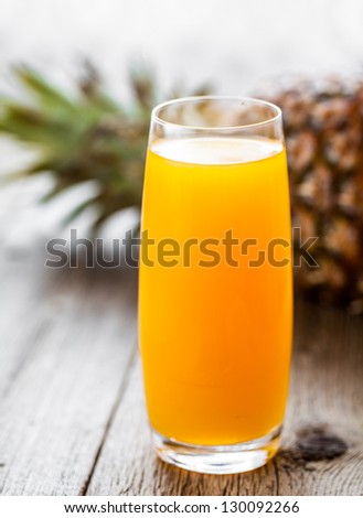 Glass of pineapple juice on wooden table.  Very shallow depth of field (focus on the front edge).