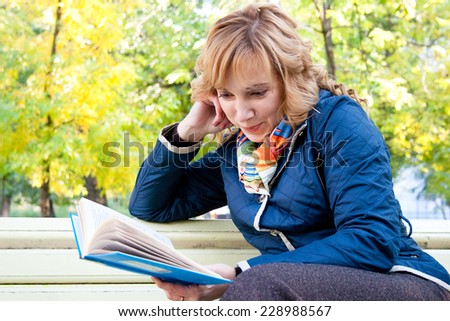 Portrait of a young blond woman reading a book in the autumn park