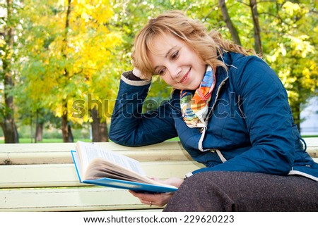 Portrait of a young blond woman reading a book in the autumn park
