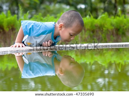The little child plays with his self reflection in a small pond.