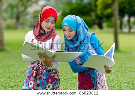 Young pretty Asian muslim college girls having discussion with book references.