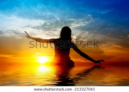 Silhouette of woman performs as yoga exercise on the beach during sunset. digital compositing, colour tone, water reflection and ripple effects.