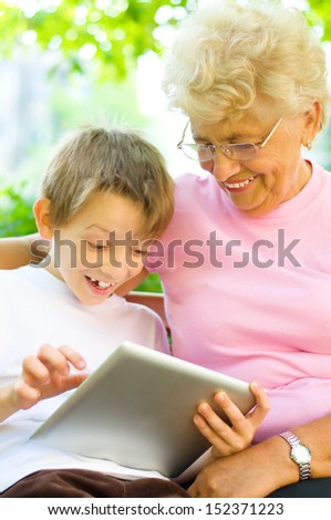 little boy with his grandmother using tablet PC, sitting in the park