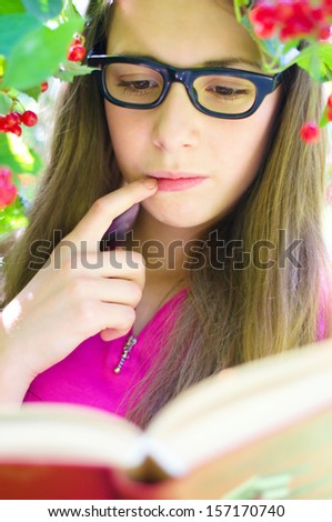 Cute teenage girl is reading a book while wearing glasses outdoors