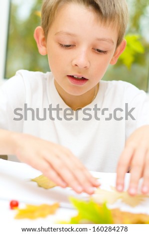 little boy applying a dry maple leaves using glue while doing arts and crafts in school