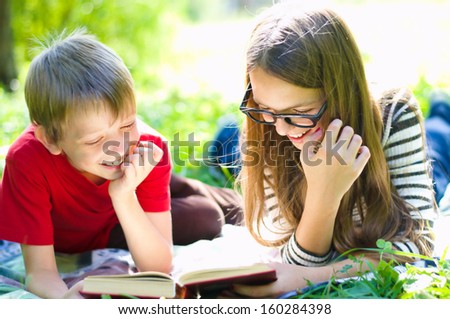 Kids reading together enjoying a book laying on the grass outdoors