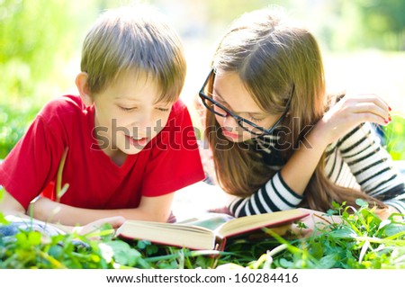 Kids reading together enjoying a book laying on the grass outdoors