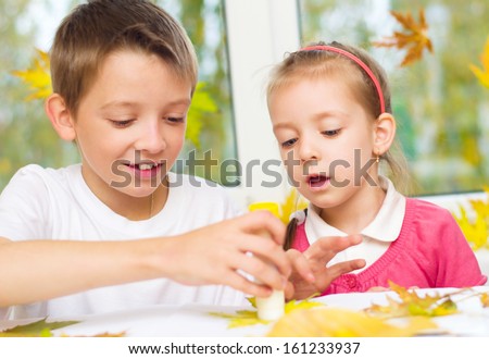 little girl with her brother applying a dry maple leaves using glue while doing arts and crafts