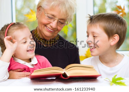 Great-grandmother reading a book for grandchildren at home
