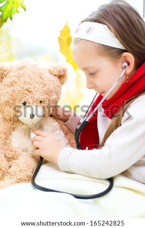 Little girl is examining her teddy bear using stethoscope