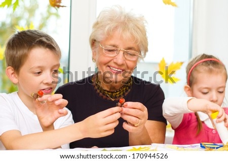 Grandmother with grandchildren applying a dry maple leaves using glue while doing arts and crafts