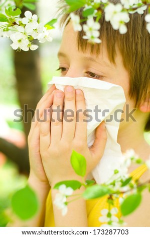 Allergy.Little boy is blowing his nose outdoors