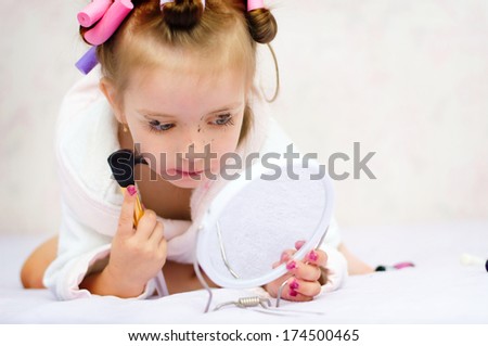 little girl painting lips while wearing hair-rollers and bathrobe