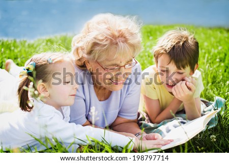 grandmother reading book to grandchildren outdoors