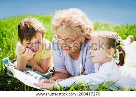grandmother reading book to grandchildren outdoors