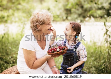 granddaughter is feeding her grandmother with cherries in the garden