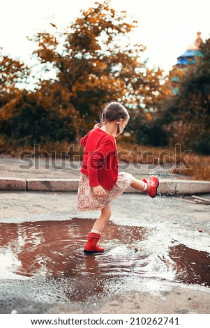 cute little girl wearing red rain boots jumping into a puddle