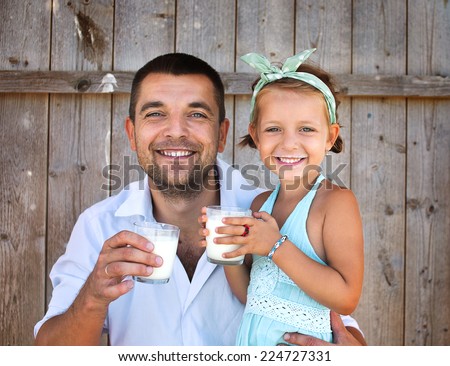 Cute little girl with his father holding  glasses of milk over wooden background