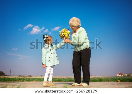happy granddaughter giving flowers to grandmother outdoors