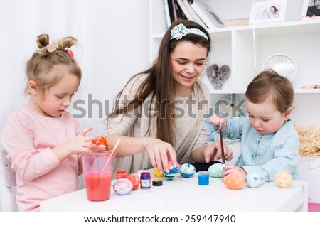 Loving mother and her little daughters painting easter eggs
