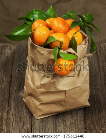 Fresh tangerines with leaves in recycle paper bag on wooden table.