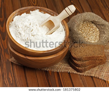 Flour in wooden bowl and wheat in burlap bag. Closeup.