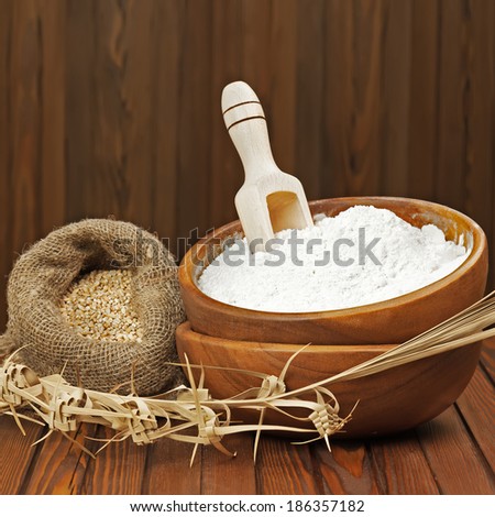 Flour in wooden bowl and wheat in burlap bag. Closeup.