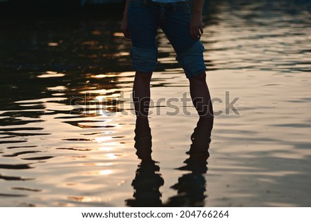 Female legs in rolled jeans in sea water on soft background of setting sun.