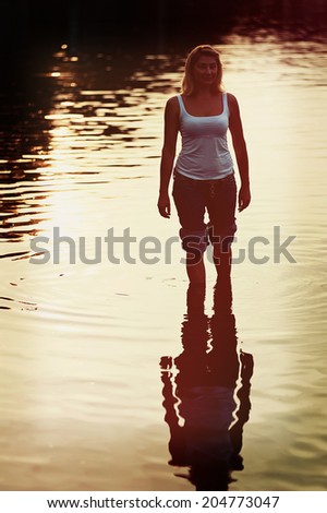 Lovely woman in jeans rolled in sea water on soft background of setting sun with retro effect filter.