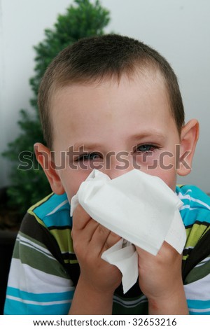 Five years old boy with tissue blowing his nose. Child with allergy, conjunctivitis and black rings round his eyes.
