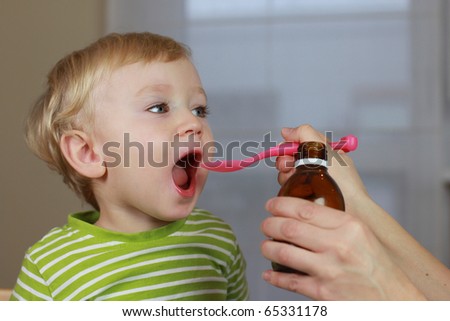 Mother giving 2 years old baby boy medicine, cough syrup on a spoon. Sick child.
