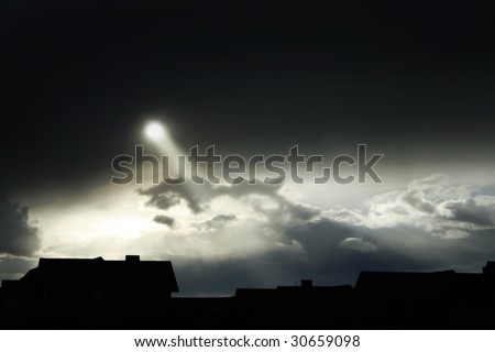 A roof-line silhouette against a dark, ominous sky.  A beam of sunlight breaks through the dark clouds.  Purposely underexposed to increase dramatization.