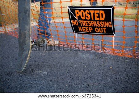 A skateboarder steps over a fence with a sign that reads \