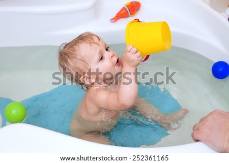 Funny little baby girl in the bath playing with water drops and splashes