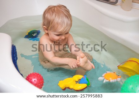 Little girl smiling  in the bathtub. Funny little baby girl in the bath playing with water drops and splashes .Girl playing with colorful toys in the bathroom