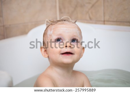 Little girl smiling  in the bathtub. Funny little baby girl in the bath playing with water drops and splashes .A child with a head in the foam shampoo
