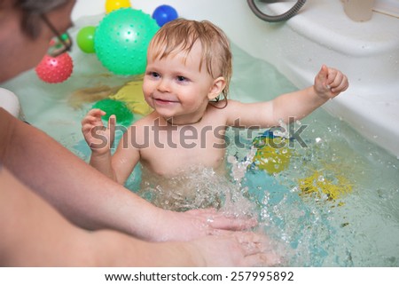 Funny little baby girl in the bath playing with water drops and splashes  Little girl smiling and playing in the bathtub with her parents. cooperative games. Fathers and Sons