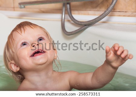 Funny little baby girl in the bath playing with water drops and splashes . Face close up