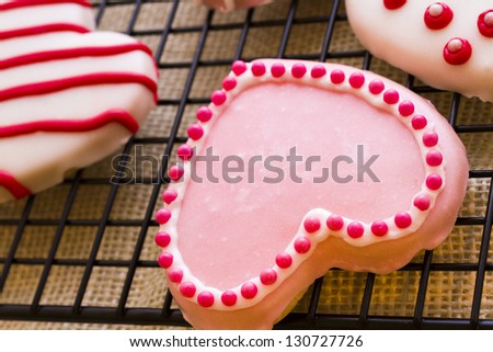 Gourtmet heart shaped cookies decorated for Valentine\'s Day on drying rack.