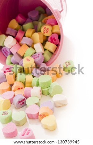 Conversation heart candies spilled from pink bucket.