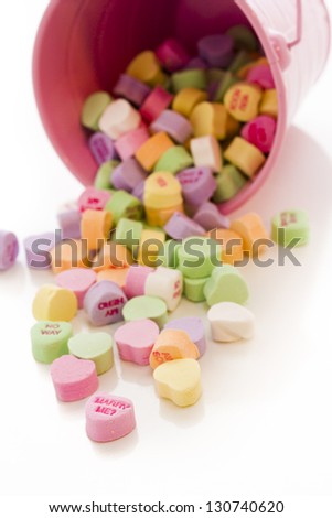 Conversation heart candies spilled from pink bucket.