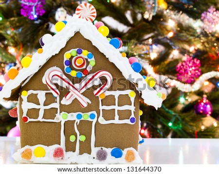 Gingerbread house decorated with candies with Christmas tree in the backgound.